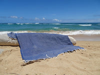 Donkerblauwe hamamdoek met wafelstructuur over een aangespoeld stuk hout op het strand bij zee